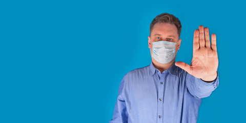 The concept of a coronavirus. The man puts on a mask to protect against the disease and shows a stop gesture with his hands to install the COVID-19 flash. A global call to stay home. Selective focus