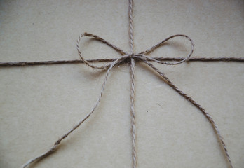 Close up picture of jute bow on dark brown background. Packing a gift for someone special. Recycle tread. String tied in a bow, over brown paper packaging. Twine tied in a bow.