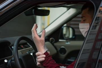 a man driving in medical mask in car puts medical gloves on a  during an epidemic, a taxi driver in a mask, protection from the virus. Driver in black car. coronavirus,infection, quarantine, covid-19