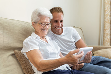 older woman with white hair and glasses sitting with a young boy watching and listening through the technologies