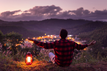 Young man with arms raised, feeling free and enjoying life. Watching the city lights with twilight...