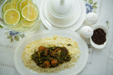 A bowl of white ceramic salt and pepper. Shah pilaf. Khan pilaf in a pita. Black pepper in a white ceramic pot . There is meat and plum chestnuts on the pilaf . Rice in a white plate. Sliced lemon .