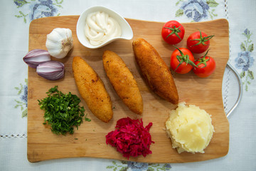 Ukrainian tradition food on a wooden board . Red cabbage sauerkraut in a small bowl . mashed potatoes . Mayonnaise, Garlic, Onion, Tomatoes. Chopped coriander.Chicken Kiev cutlets with parsley leaves.