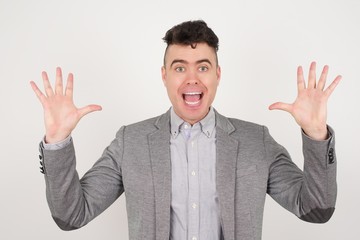 Achievement, success concept. Cheerful young male raising his hands up, having eyes full of happiness rejoicing his great achievements. Attractive caucasian male dressed formally.