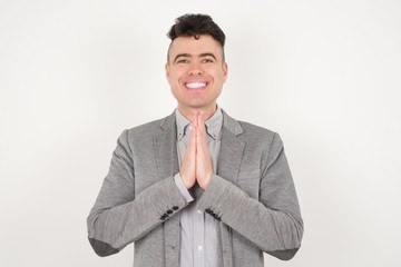 Horizontal portrait of pretty blond man keeps palms together, has pleased expression. Glad attractive male makes request, pleads for mercy. Hopeful young adult.