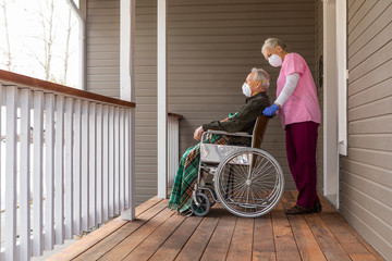 Woman and man in wheelchair wearing protective mask to prevent coronavirus transmission on porch