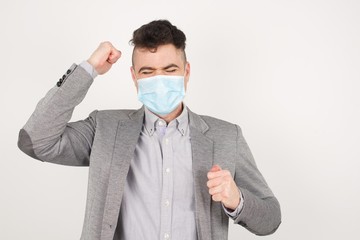 Attractive young caucasian man celebrating a victory punching the air with his fists and a beaming toothy smile over a gray studio background with copy space