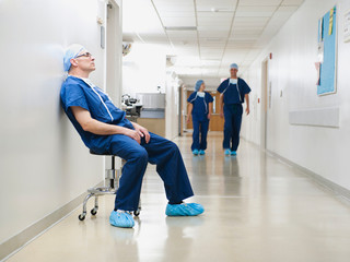 Surgeon resting in hospital corridor after operation, while two of his colleagues are walking in background
