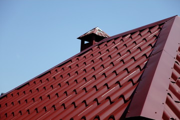Chimney. Chimney on the roof of a house made of red-brown metal tile with a fungus on top.