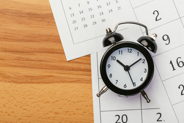 Flat lay or top view of black alarm clock with white calendar on wooden  board with copy space,...