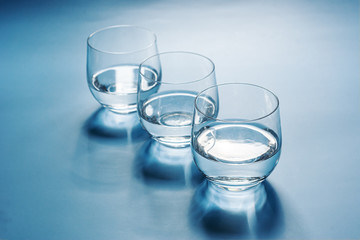 Three glasses of water with soft shadows on a blue background. Freshness and purity, concept