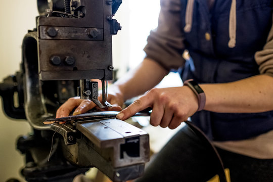Female saddler standing in workshop, sewing leather strap on saddlery sewing machine.