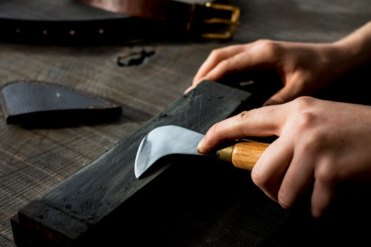 High angle close up of person sharpening saddle making tool on whetstone.