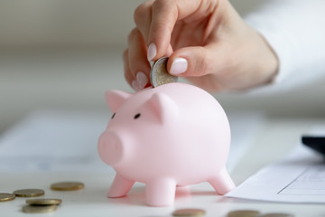 Close up crop view of female put coin in pink piggy bank saving money for future, provident practical woman housewife manage household finances expenditures, feel economical about home expenses