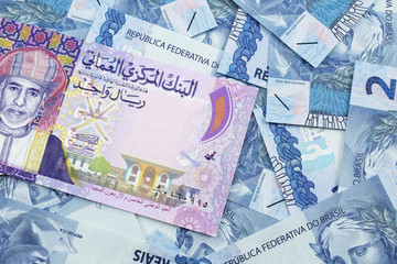 A close up image of a colorful one rial bank note from Oman on a bed of Brazilian two reais bank notes in macro