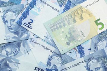 A close up image of a five Euro bank note from Europe in macro with a bed of Brazilian two reais bank notes