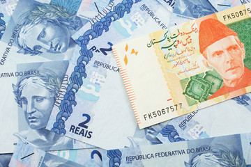 A close up image of a orange and green twenty Pakistani rupee bank note with Brazilian two reais bank notes in macro