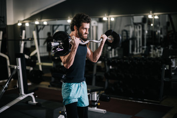 Fototapeta na wymiar Handsome bearded young man with muscular wiry body wearing sportswear working out with barbell during sport workout training in modern dark gym. Concept of healthy lifestyle.