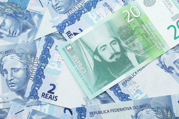A close up of a green and white, twenty Serbian dinar bank note on a background of Brazilian two reais bank notes