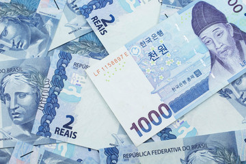 A blue South Korean one thousand won bank note close up in macro on a background of Brazilian two reais bank notes