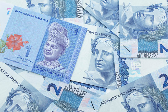 A close up image of a blue one Malaysian ringgit bank note on a bed of Brazilian two reais bank notes close up in macro