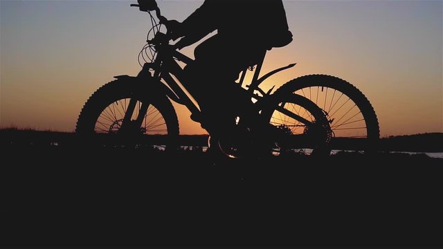 Cinematic shot silhouettes of two cyclists riding mountain bicycles near river on sunset slow motion. Sport and healthy lifestyle concept