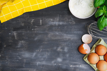 Baking cooking ingredients: flour, eggs and kitchen textile. Black background. Top view copy space.