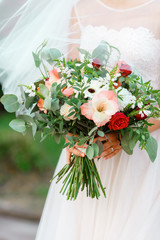 Elegant bride in a white wedding dress with lace and veil holding in hands delicate, expensive, trendy bridal bouquet of flowers in white and red colors.Vegetative floral style