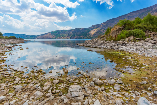 Mirror water surface. Panoramic view of Ili Lake of Nemrut volcano, Bitlis Province, Eastern Turkey. Reflection of the cloudy sky in the lake. Stone bottom through clear water