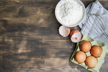 Baking cooking ingredients: flour, eggs and kitchen textile. Wooden background. Top view copy space