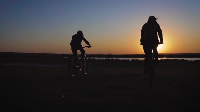 Family of two people having ride together in rural landscape. Son and mother pedaling bikes over sunset blue sky background in slow motion. Sport and healthy lifestyle concept