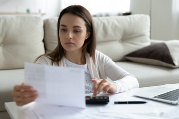 Focused young Caucasian woman manage household finances expenditures calculate taxes on machine,...