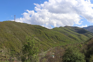 Fototapeta na wymiar Armenia. There are many hills near the town of Kapan. In spring, all nature turned green. Without leaves yet nut trees. Over the hills spring clouds and blue sky.