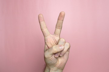 Male hand with fair skin shows a gesture, hand on a light pink background. Victoria hand or number two. Stock photo for web and print. 