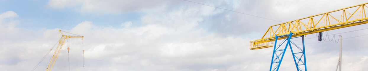 Obraz premium Machine crane and bridge crane on a background of blue sky with clouds, panoramic view, high resolution