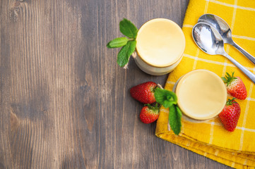 Two glasses of natural yogurt on a wooden table are decorated with mint and strawberries.