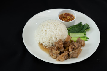 Stewed pork with rice, spicy sauce and vegetables. Black background 