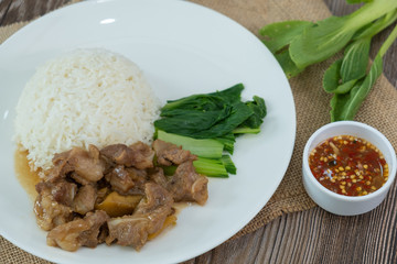 Stewed pork with rice, spicy sauce and vegetables. Wooden table
