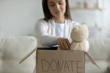 Close up of young Caucasian woman put clothes things into cardboard box make volunteer donation to...