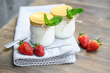 Two glasses of natural yogurt on a wooden table are decorated with mint and strawberries.