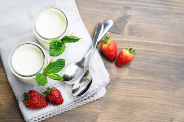 Two glasses of natural yogurt on a wooden table are decorated with mint and strawberries.