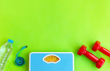 Sports and workout equipment on green background top view with water,measuring tipe, dumbbells, floor scales, weight loss and physical activity concept, mockup copy space