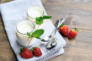 Two glasses of natural yogurt on a wooden table are decorated with mint and strawberries.