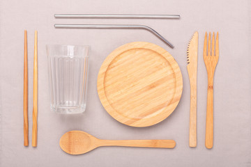 Zero waste, plastic free concept. Wooden plate, glass cup, Set of bamboo cutlery. Flat lay on textile linen background