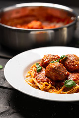Spaghetti meatball portrait side view. Italian pasta dish served in white plate on black wooden background. Spaghetti and meatballs is like bolognese sauce with balls of meat cooked in tomato sauce.