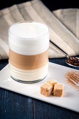 Glass Cup of coffee latte with foam on a blue wooden table with sugar and a napkin