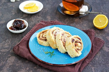 Dessert, sliced sponge cake with plum jam on a blue plate on a brown concrete background.