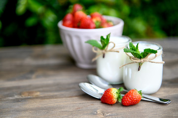 Two glasses of natural yogurt with chia on a wooden table are decorated with mint and strawberries.