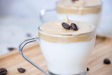 Close up of a crystal glass with milk and whipped instant coffee with raw coffee beans on a bamboo tray and a white background with depth of field. Dalgona coffee concept