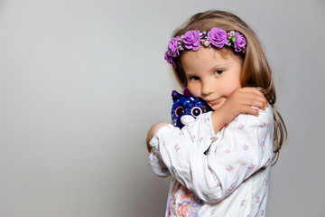 Portrait of sad little girl  in white dress and purple wreath with plush unicorn toy on gray isolated background. Look at camera 